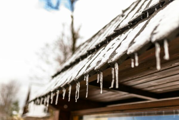 Hanging icicles from the roof of a wooden building on a winter frosty day, a lot of snow on the roof